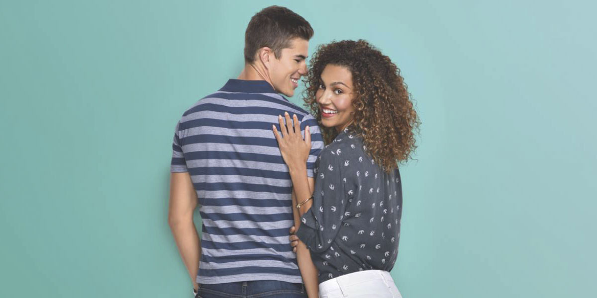 Young man in a blue stripped polo and woman wearing a blue blouse standing backwards and smiling.