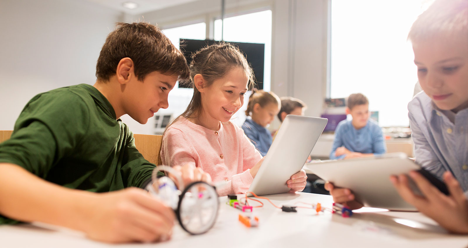 Kids gathered around computers engaged in learning.
