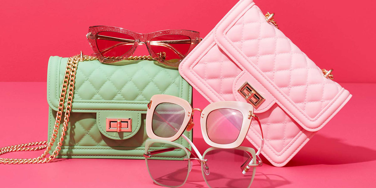 Pink and green clutch purses and two pairs of fashionable sunglasses on a pink background.