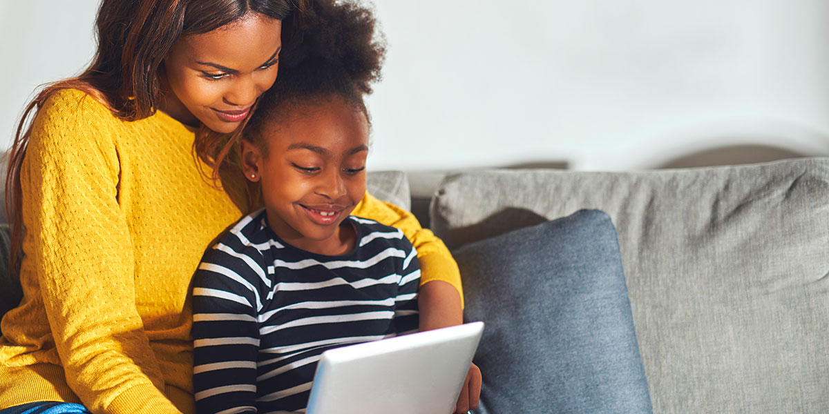 Black mother and child sitting on a couch watching a tablet.